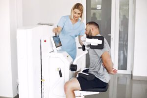 Patient has a rehabilitation in physiotherapy clinic.  A therapist helps him. People are in the gym.
